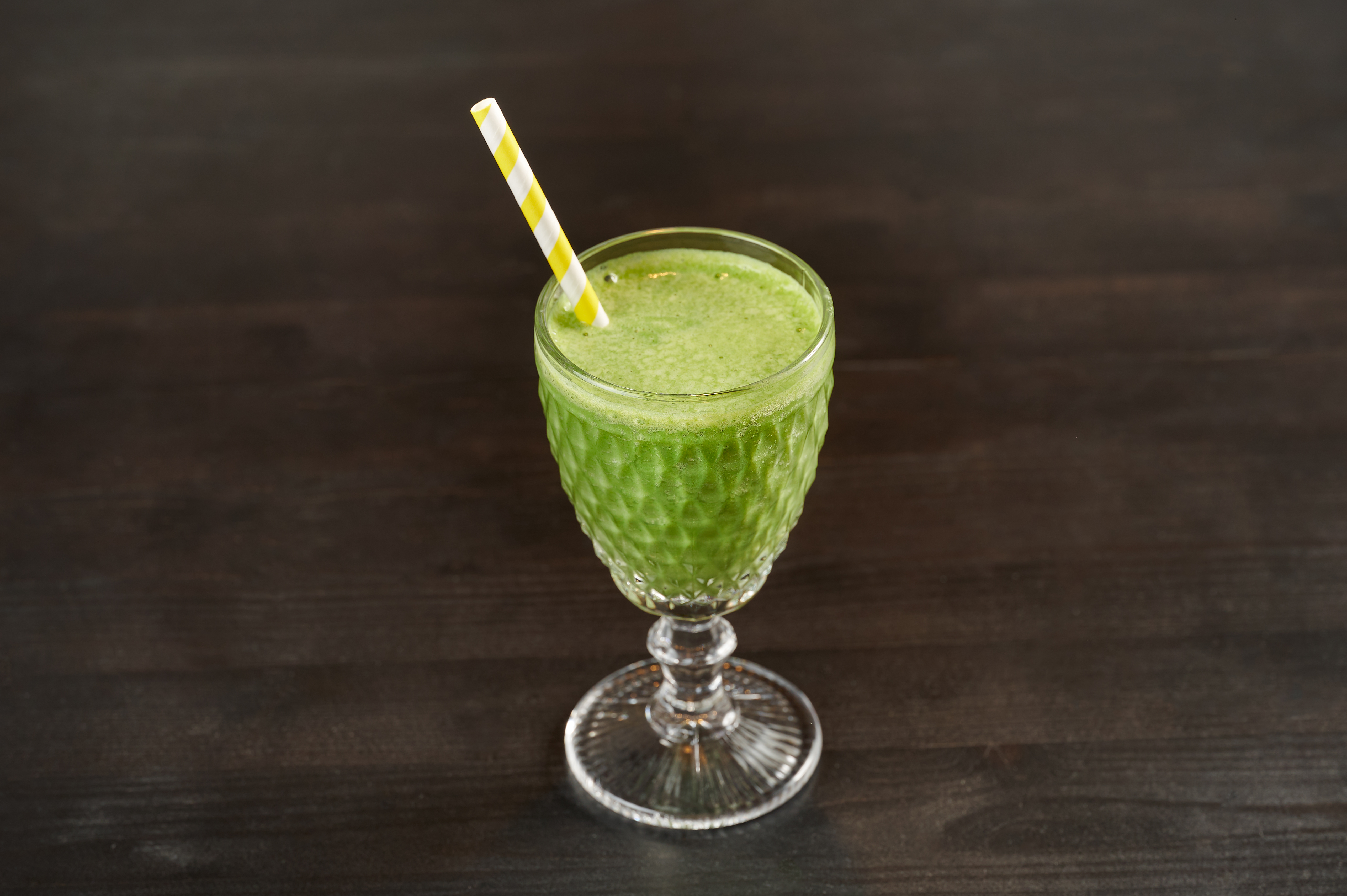 Green smoothie in a crystal glass with a paper straw